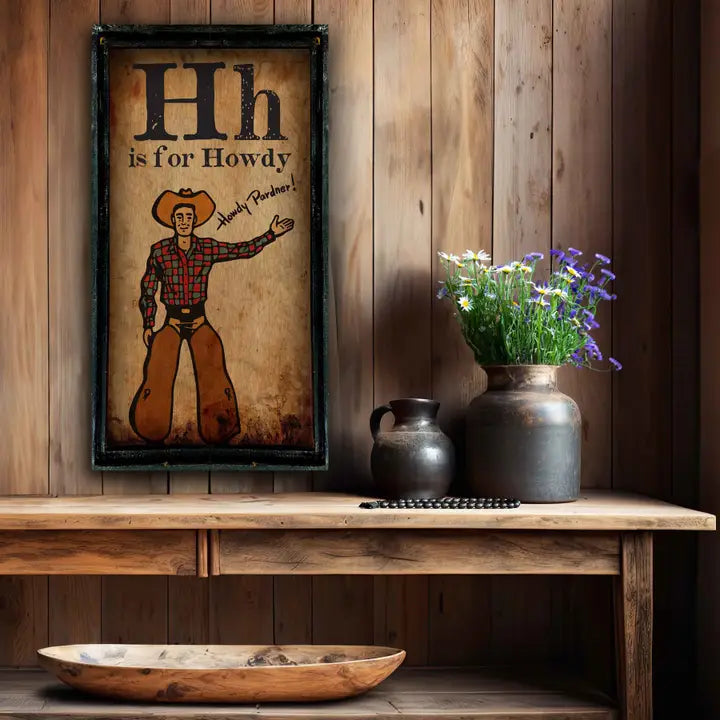Decorative shelf with western wall art featuring 'Hh is for Howdy' and a cowboy, vases, and a bowl against a wooden wall.
