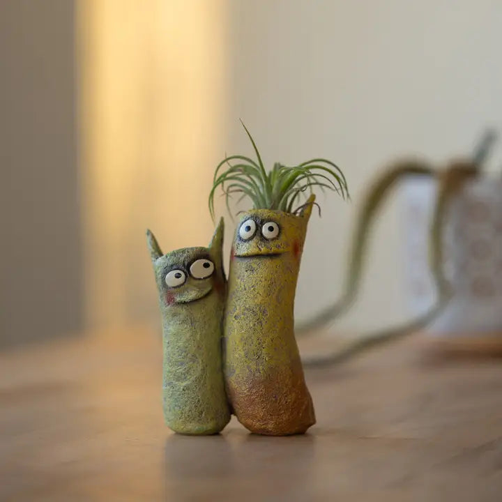 Two small, cat-shaped plants with googly eyes on a wooden surface.