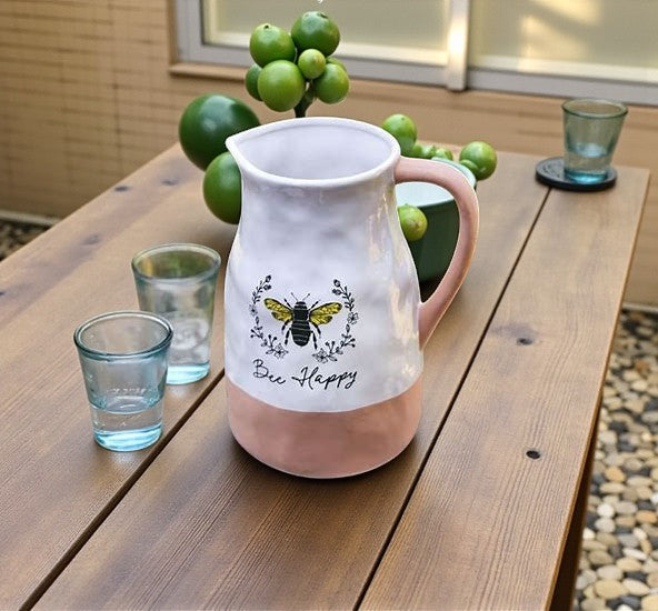 Pink pitcher with 'Bee Happy' design on a wooden table with glasses and limes.